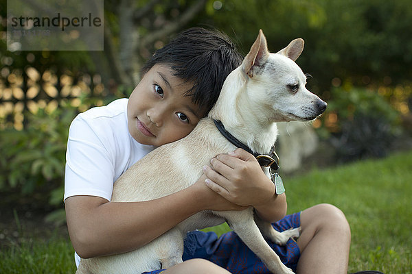 Gemischtrassiger Junge umarmt Hund im Freien