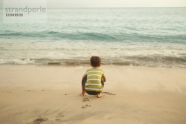 Gemischtrassiger Junge hockt am Strand und spielt