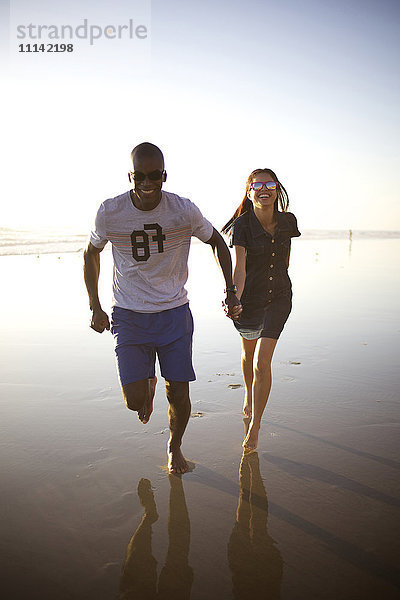 Glückliches Paar hält Hände und läuft am Strand