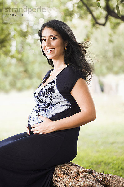 Gemischtrassige schwangere Frau  die im Freien sitzt
