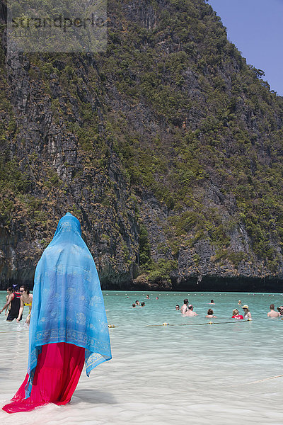 Frau mit traditionellem Kopftuch steht am Strand