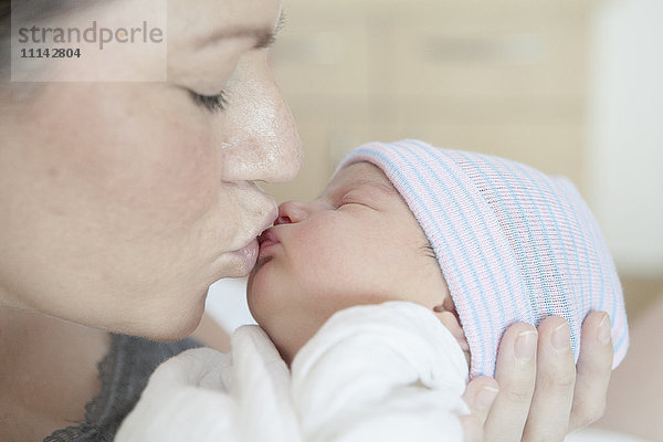 Kaukasische Mutter küsst neugeborene Tochter