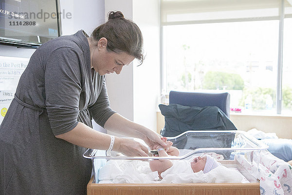 Kaukasische Mutter wickelt ihre neugeborene Tochter im Krankenhausbettchen