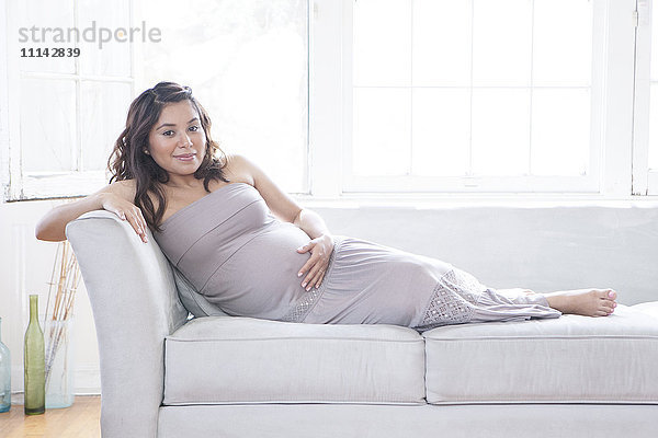 Schwangere hispanische Frau mit Bauch auf dem Sofa