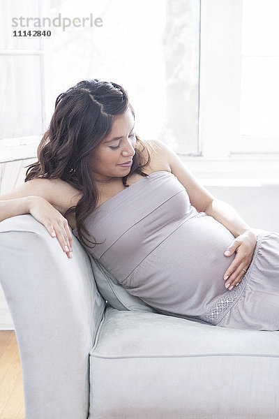 Schwangere hispanische Frau mit Bauch auf dem Sofa