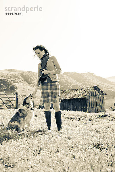 Frau streichelt Hund in ländlicher Landschaft