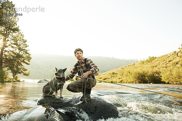 Mann mit Hund beim Angeln im Fluss