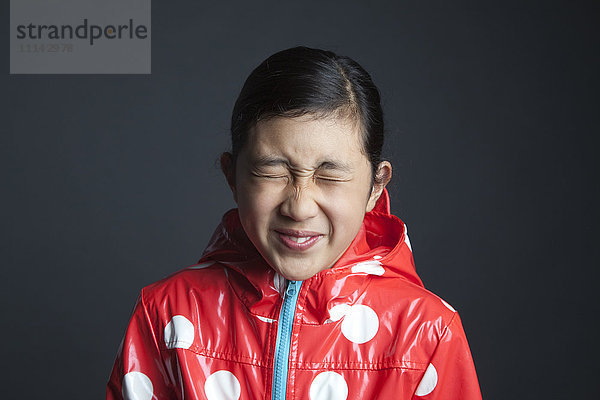 Blinzelndes asiatisches Mädchen mit Regenmantel