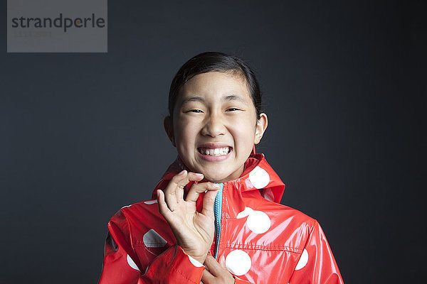 Lachendes asiatisches Mädchen  das den Reißverschluss des Regenmantels schließt