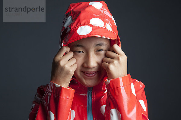 Lächelndes asiatisches Mädchen in einem Regenmantel mit Kapuze