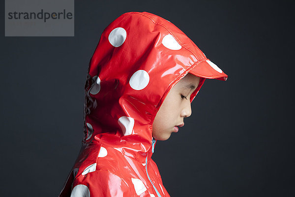 Enttäuschtes asiatisches Mädchen in einem Regenmantel mit Kapuze