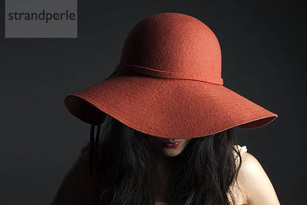 Asiatische Frau versteckt sich hinter rotem Hut