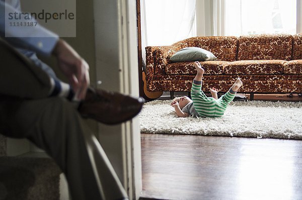 Geschäftsmann bindet Schuhe  während sein Sohn im Wohnzimmer spielt