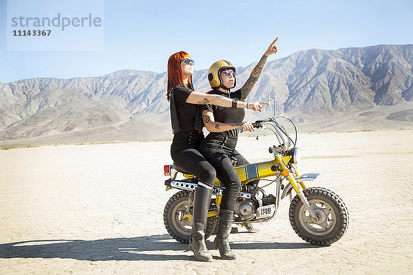 Frauen auf einem Motorrad in der Wüste sitzend