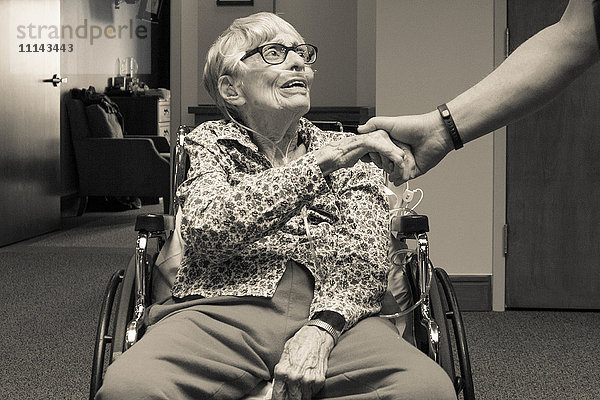 Ältere Frau im Rollstuhl schüttelt die Hand eines Mannes