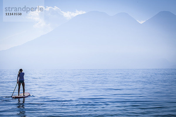 Mädchen steht auf einem Paddelbrett in einem abgelegenen See