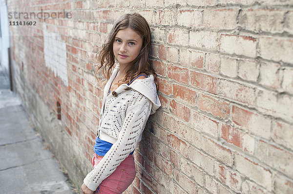 Lächelndes Mädchen lehnt an einer Backsteinmauer