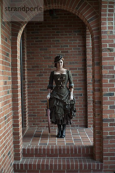 Frau in altem Kleid in gemauertem Torbogen