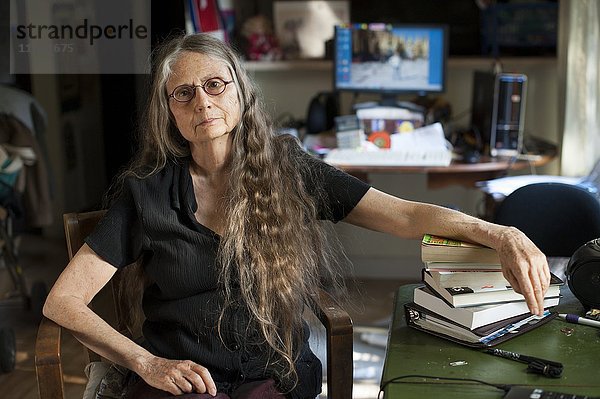 Ältere Frau stützt sich auf einen Bücherstapel am Schreibtisch