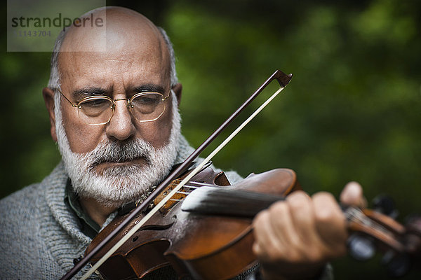 Älterer kaukasischer Mann spielt Geige im Freien