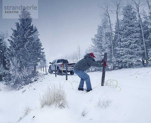 Mann repariert Holzpfosten im verschneiten Boden