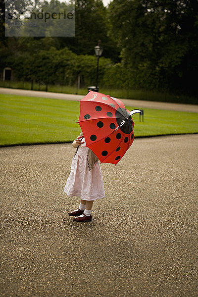 Mädchen steht unter Regenschirm im Park