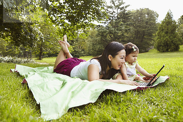 Mutter und kleines Mädchen benutzen Laptop im Park