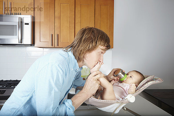 Vater küsst die Füße des Babys im Stuhl