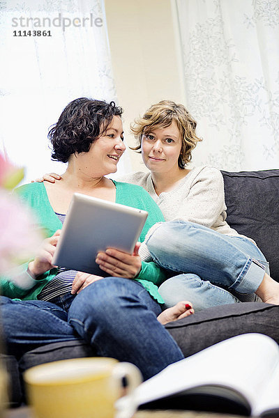 Lesbisches Paar benutzt digitales Tablet auf Sofa im Wohnzimmer