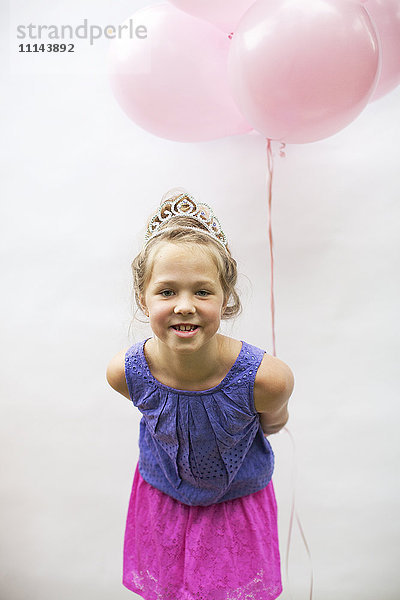 Lächelndes Mädchen mit Tiara und rosa Luftballons