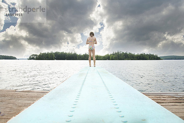 Kaukasisches Mädchen steht auf einem Sprungbrett über einem See