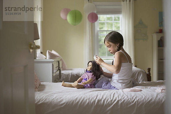 Kaukasisches Mädchen bürstet die Haare einer Puppe auf dem Bett