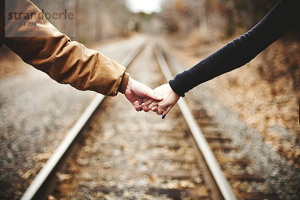 Nahaufnahme eines sich an den Händen haltenden Paares auf Bahngleisen