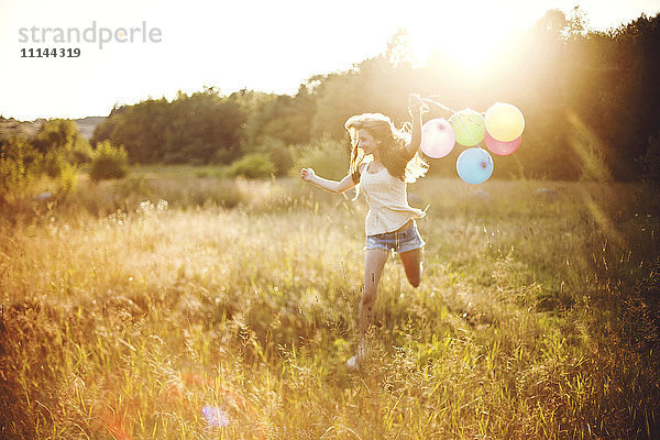 Mädchen läuft mit Luftballons in einem sonnigen Feld