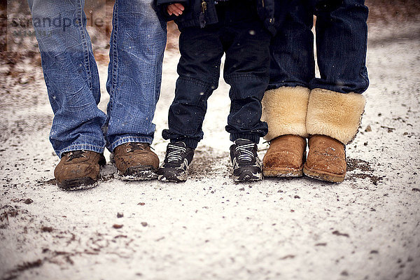 Nahaufnahme der Stiefel einer im Schnee stehenden Familie