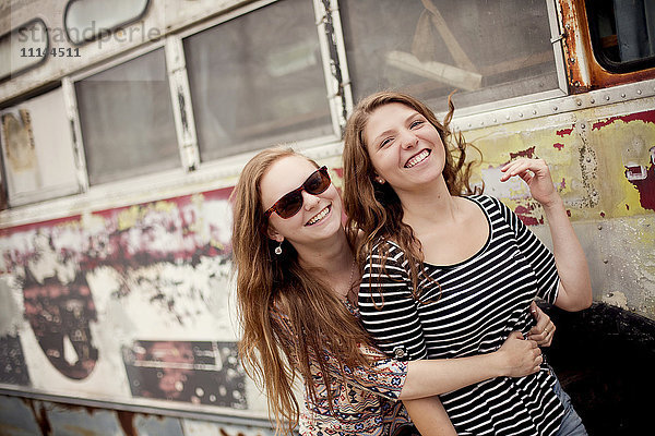 Lächelnde Mädchen  die sich in der Nähe des baufälligen Busses umarmen