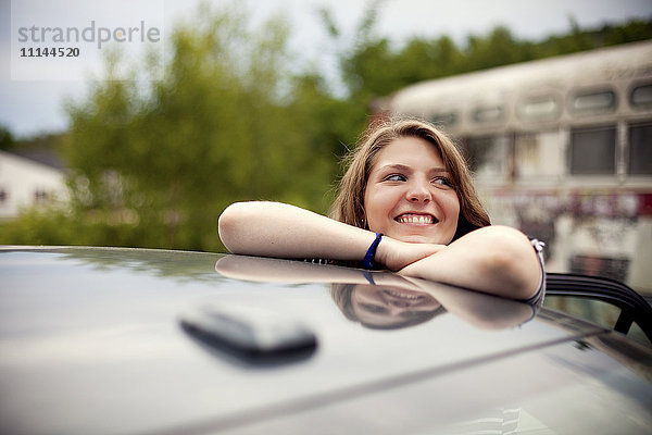 Lächelndes Mädchen lehnt auf dem Autodach