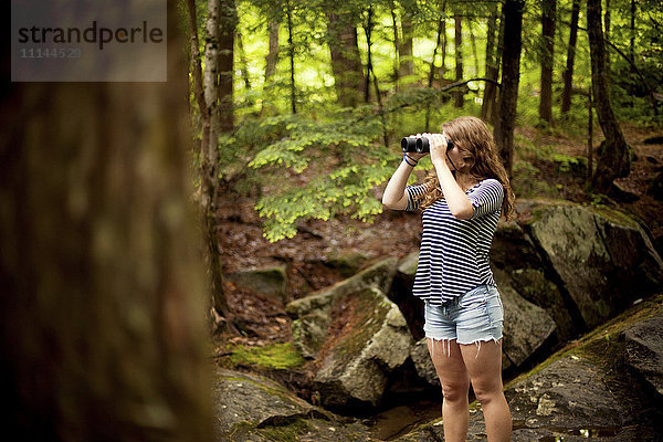 Mädchen schaut durch ein Fernglas im Wald