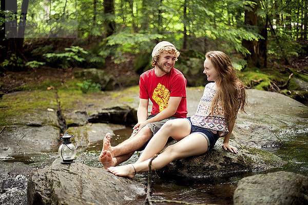 Paar sitzt barfuß auf Felsbrocken im Wald
