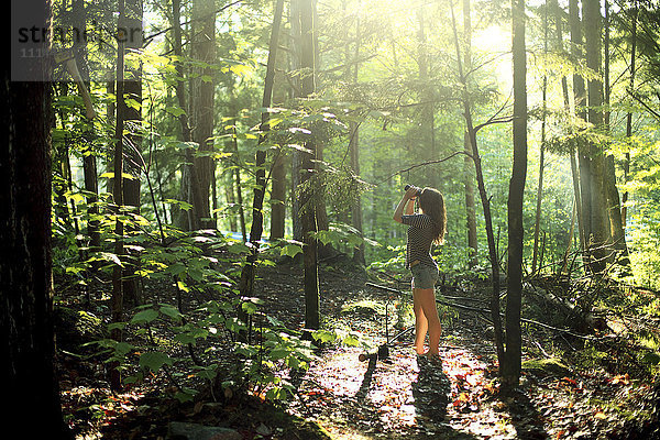 Mädchen schaut durch ein Fernglas im Wald