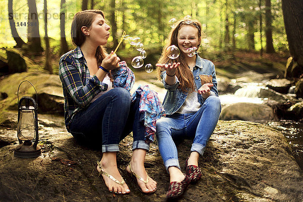 Mädchen blasen Seifenblasen auf Waldfelsen