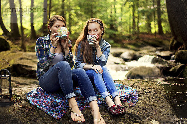Mädchen trinken Kaffee auf einem Waldfelsen