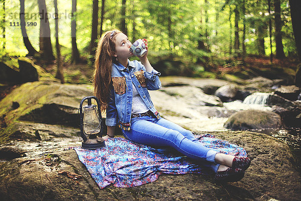 Kaukasisches Teenager-Mädchen trinkt Kaffee auf einem Waldfelsen