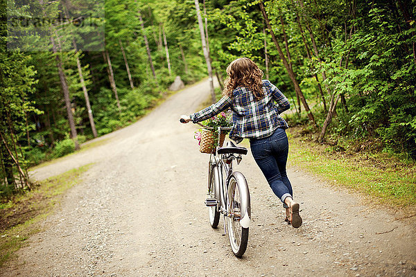 Rückansicht eines Mädchens  das ein Fahrrad auf einem Feldweg schiebt