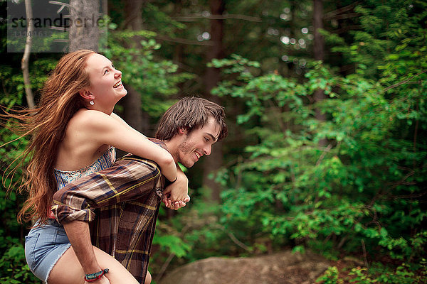 Mann trägt Freundin huckepack im Wald