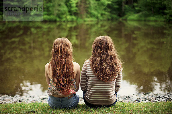 Rückansicht von Mädchen  die am See sitzen