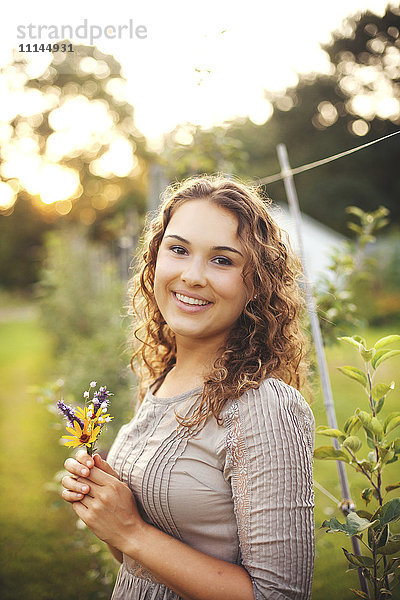 Lächelnde Frau hält Blume im Garten