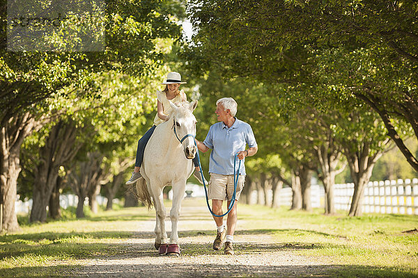 Kaukasischer Mann  der mit seiner Enkelin auf einem Pferd spazieren geht