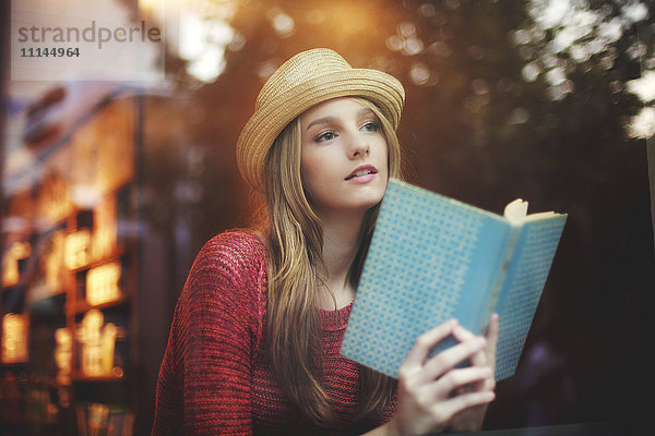 Mädchen liest Buch am Fenster
