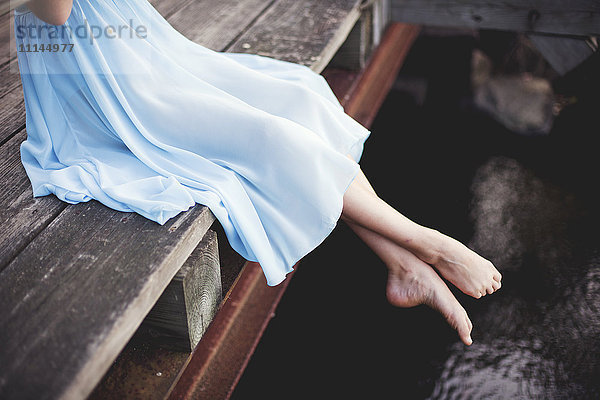 Mädchen mit baumelnden Füßen auf einem Holzsteg